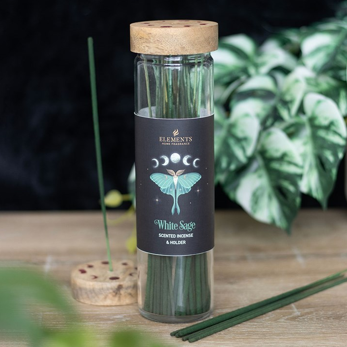 Glass bottle with wooden lid containing white sage sticks on a wooden surface with plants in the background.