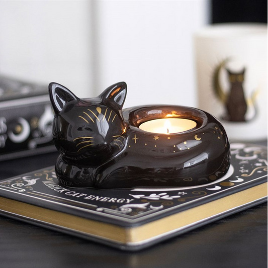 Cat-shaped candle holder with a lit candle on a book titled 'Black Cat Energy'.