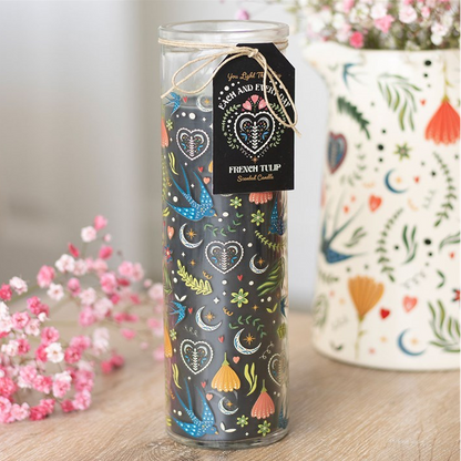 Decorative candle with colorful patterns on a wooden surface with flowers in the background