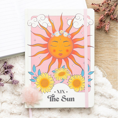 Card with a sun illustration and flowers on a white surface with floral decorations.