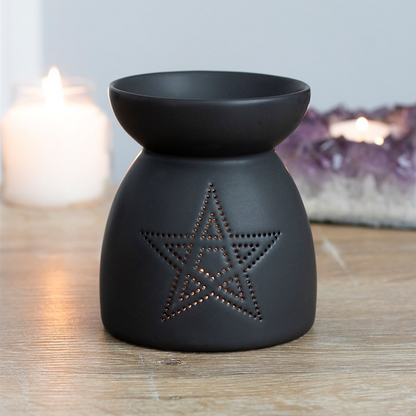 Black ceramic oil burner with star design on a wooden surface.