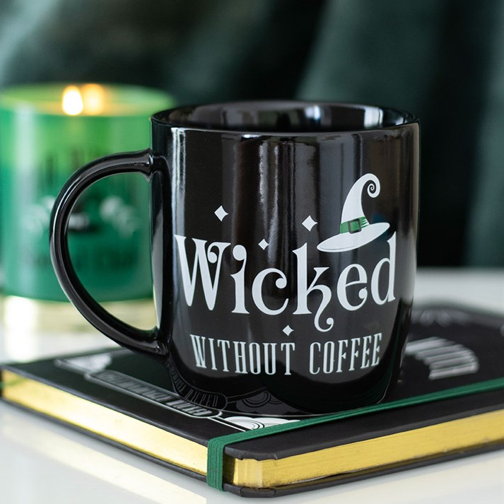 Black mug with 'Wicked Without Coffee' text on a book with a green candle in the background