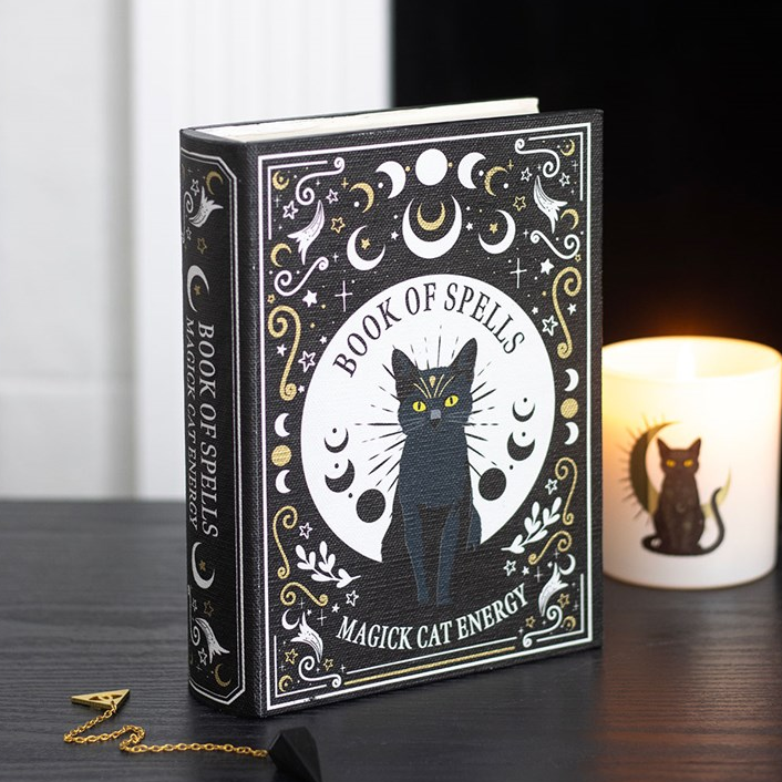 Decorative book titled 'Book of Spells: Magick Cat Energy' with a black cat illustration on a wooden surface.