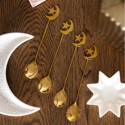 Set of gold spoons with moon and star designs on a wooden surface.