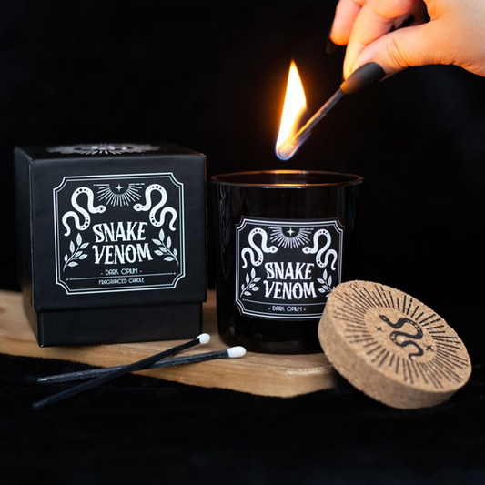 Candle labeled 'Snake Venom' being lit with packaging and lid in the background.