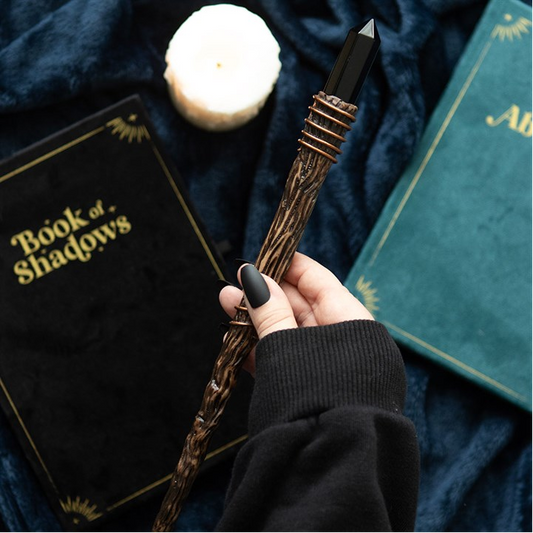 Hand holding a wand over 'Book of Shadows' with a candle and green book in the background