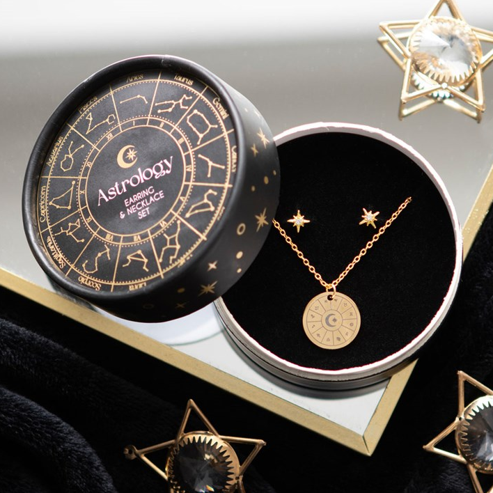 Gold necklace in an 'Astrology' branded box with decorative stars and crystals on a white background.