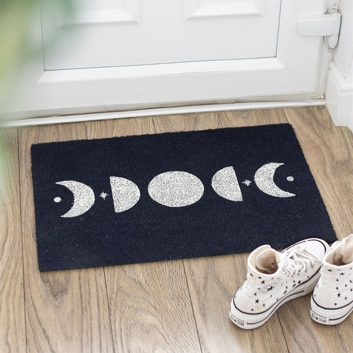 Black doormat with moon phases design on a wooden floor, shoes at the entrance.