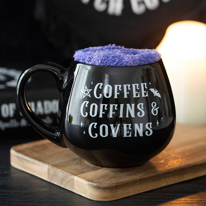 Black mug with 'Coffee, Coffins & Coven' text on a wooden surface.