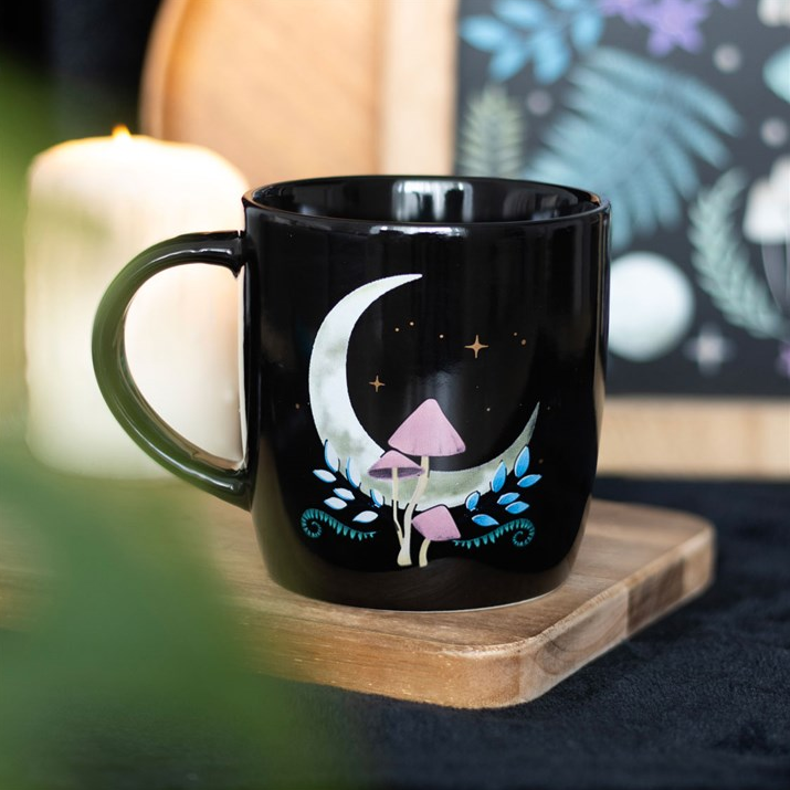 Black mug with a moon and mushroom design on a wooden coaster.
