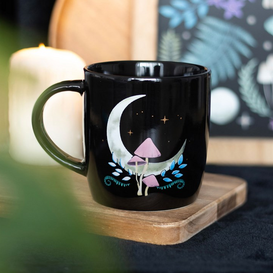 Black mug with a moon and mushroom design on a wooden coaster.