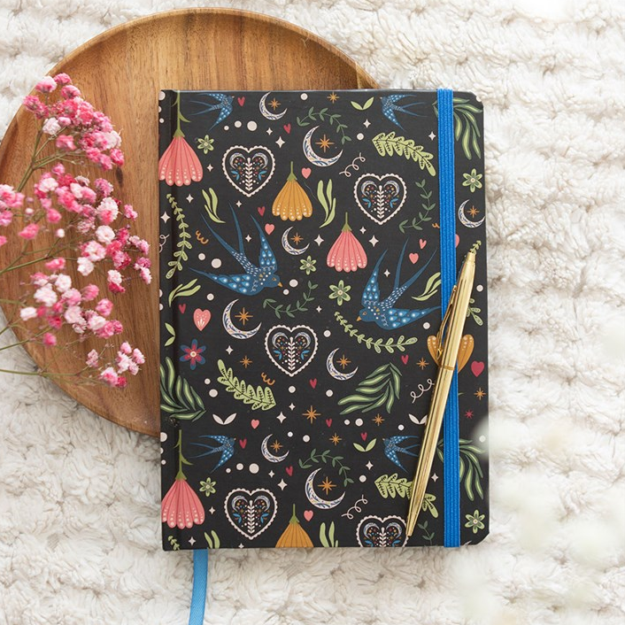 Notebook with colorful patterns on a textured surface with flowers and a wooden coaster.