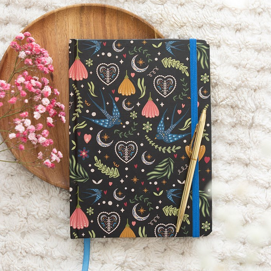 Notebook with colorful patterns on a textured surface with flowers and a wooden coaster.
