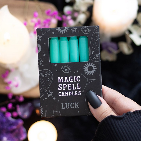 Pack of turquoise candles labeled 'Magic Spell Candles Luck' held by a hand with a blurred candlelit background.
