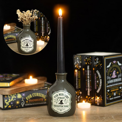 Decorative bottle with a candle inside, surrounded by books and candles on a wooden surface.
