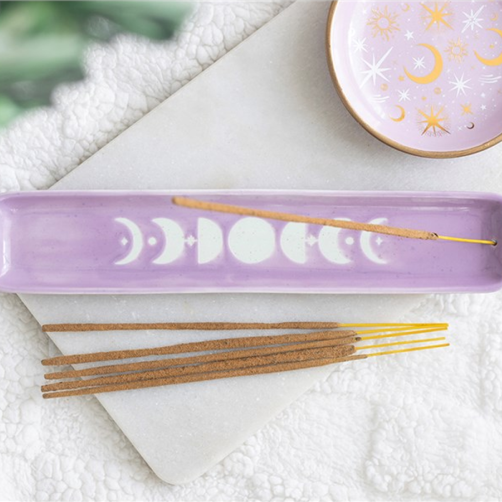 A lavender rectangular incense holder with a moon phase design, shown with incense sticks on a white marble tray and a matching decorative bowl in the background.